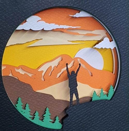 Χαρτοκοπτική εικόνα τοπίου με βουνά, ήλιο και ανθρώπινη φιγούρα